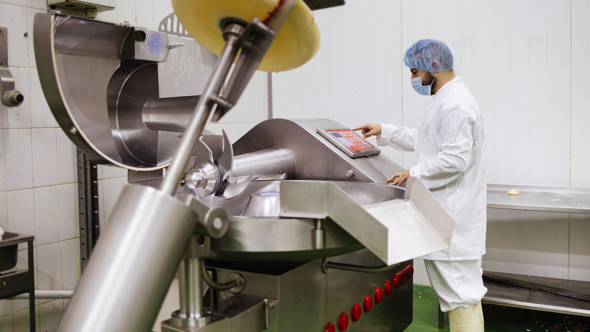 Worker in hygienic clothing operating an industrial cutter machine in food production.