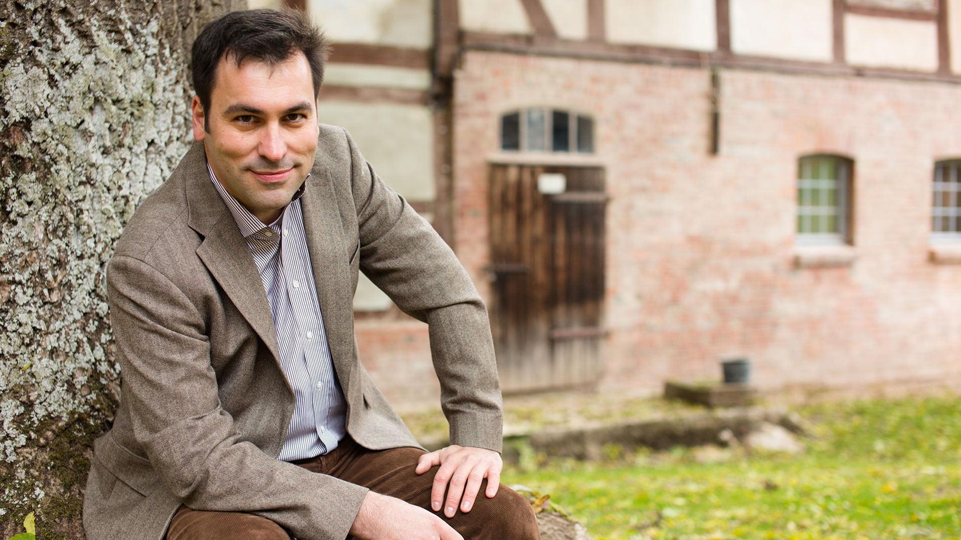 Portrait of Christian Vieth in brown jacket in front of historic farmhouse