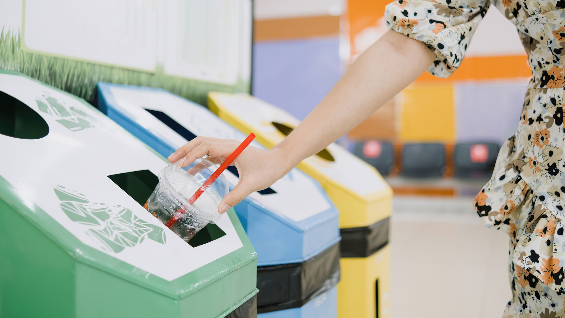 Frau entsorgt Plastikbecher in Recyclingbehälter