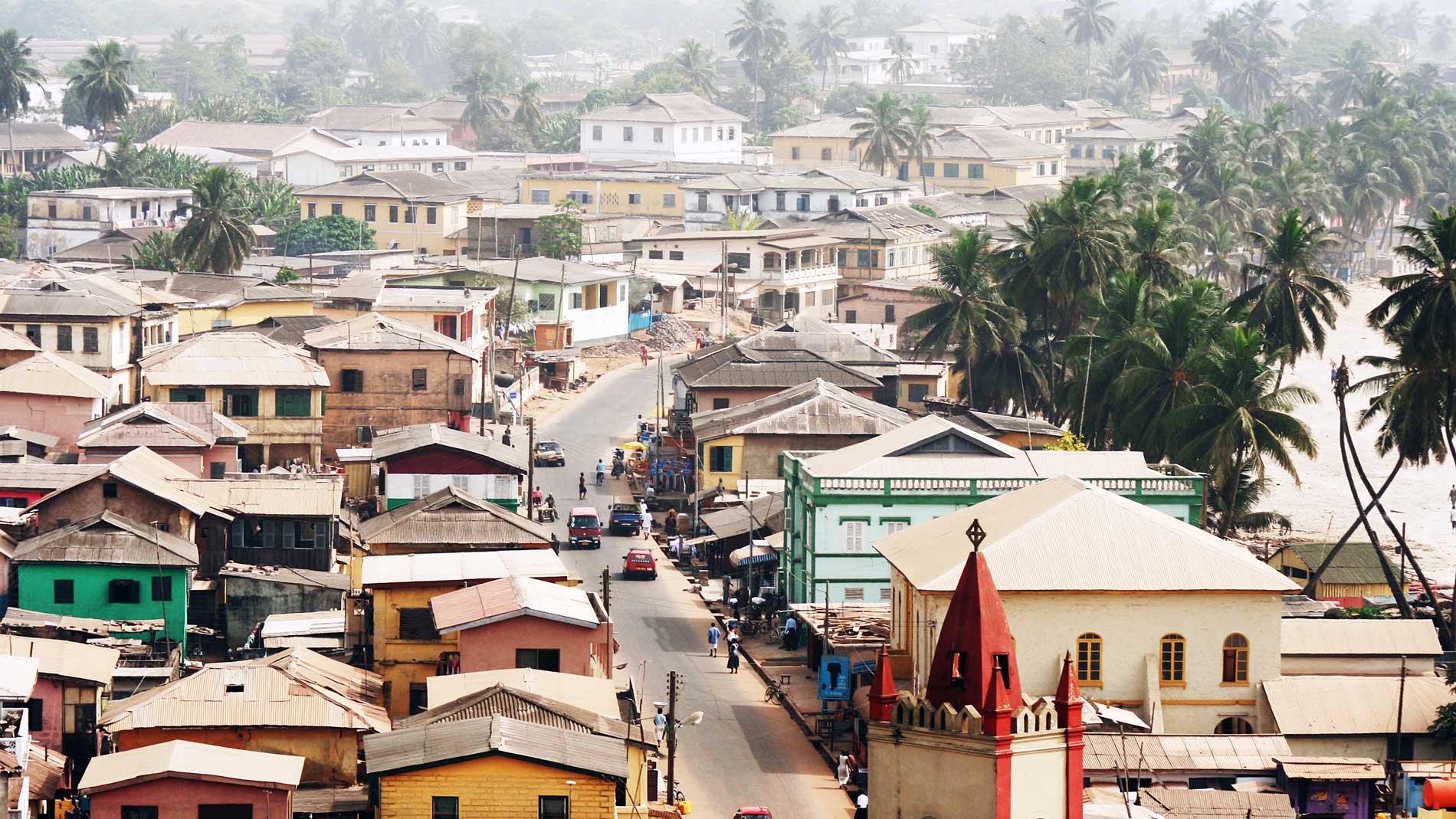 View over rooftops of a Ghanaian town with palm trees and coastline