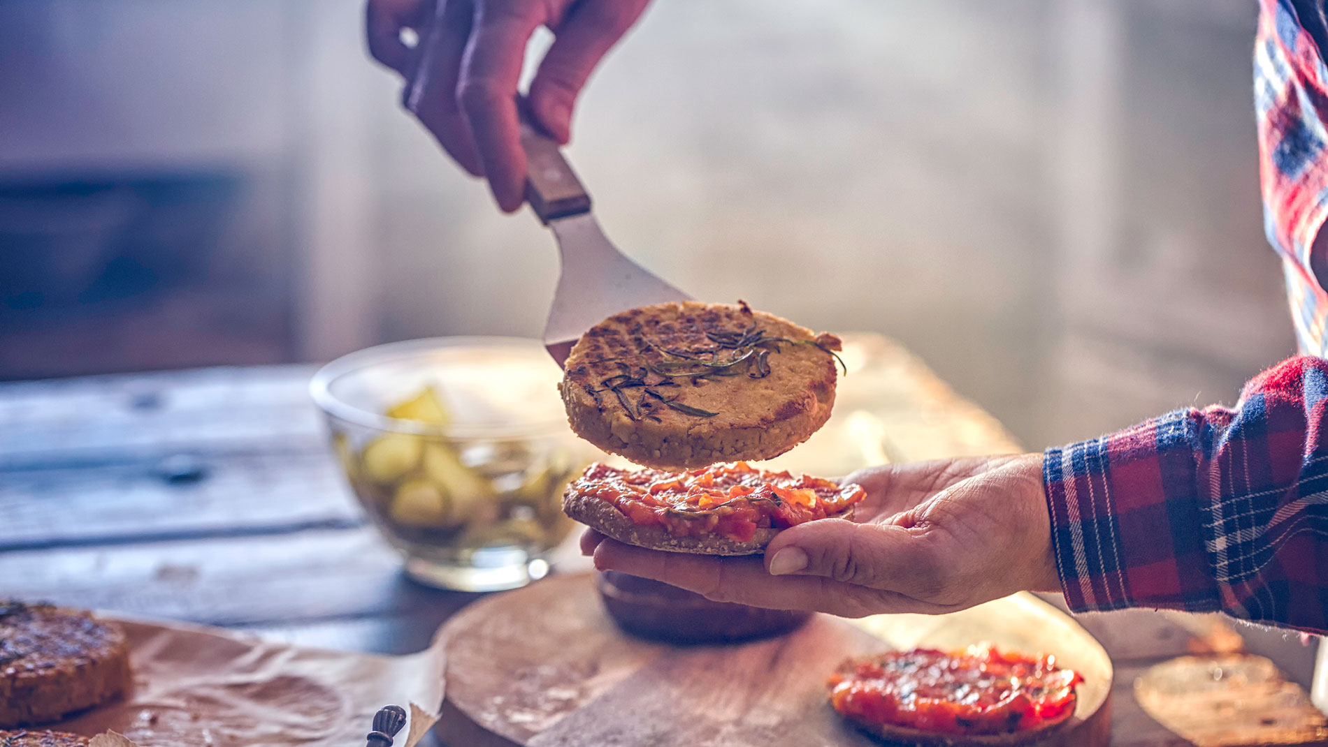 Hand holding a vegetarian burger patty over a bun with a spatula, Photo: GMVozd