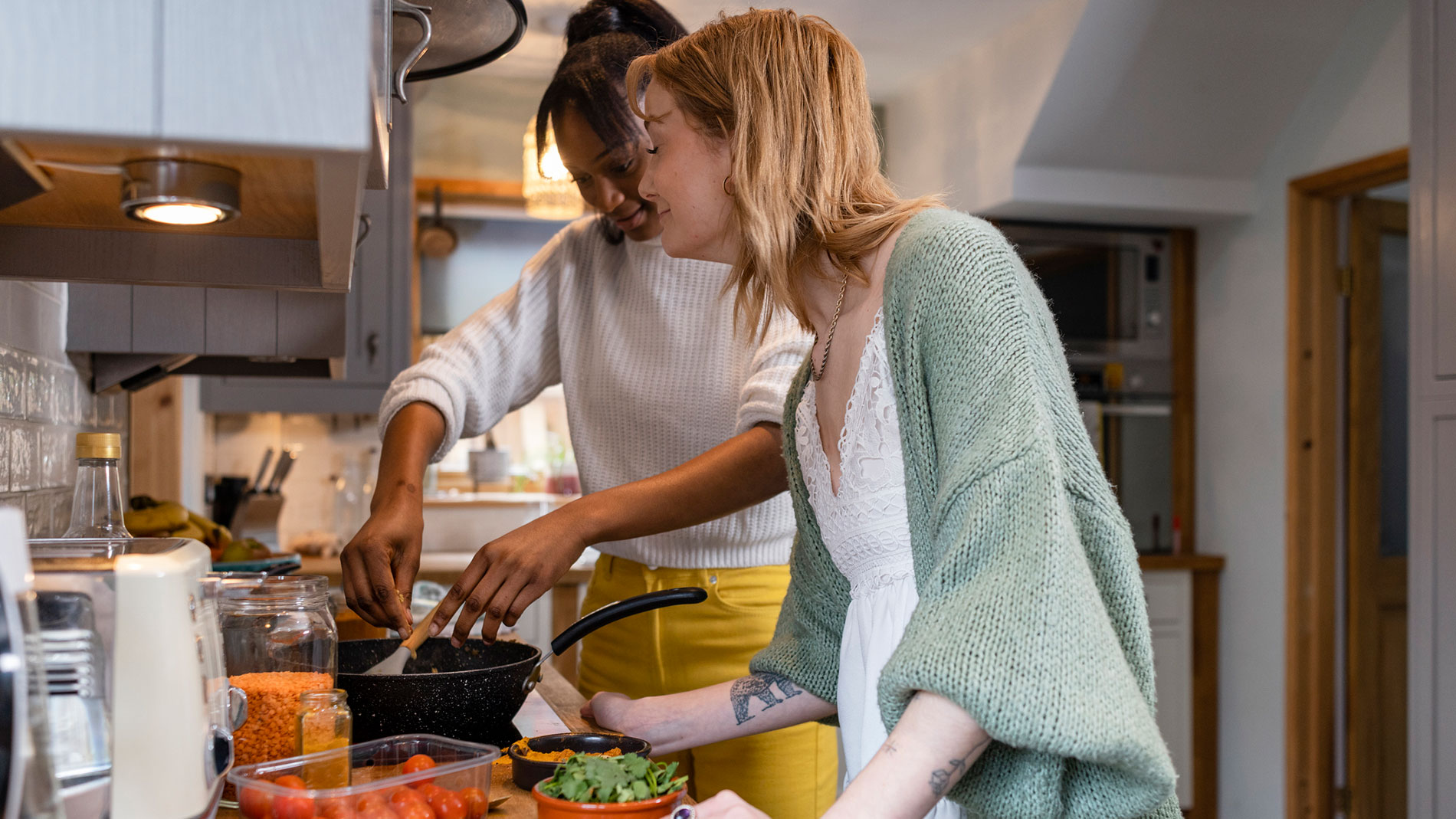 Two women are cooking together in a kitchen and stirring a pan., Photo: SolStock