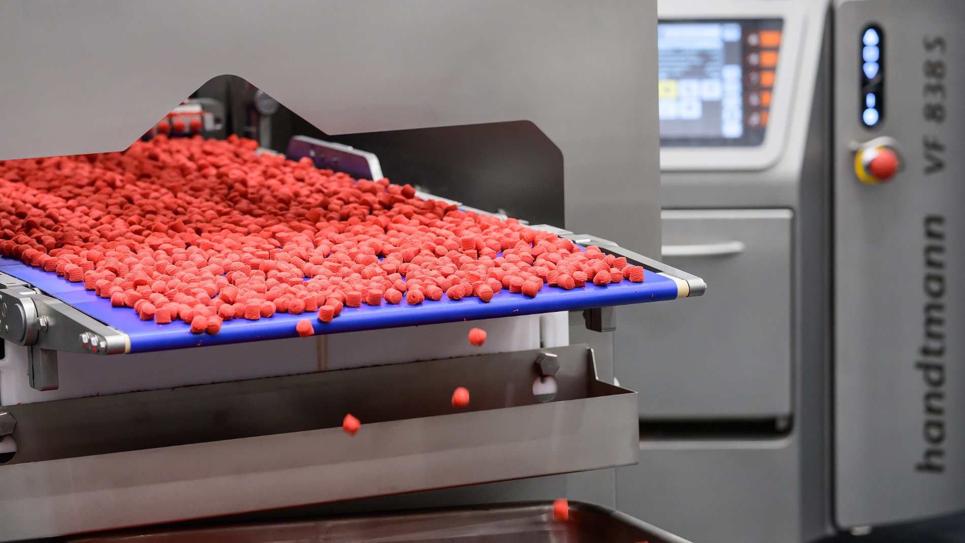Red pellets falling from conveyor into machine