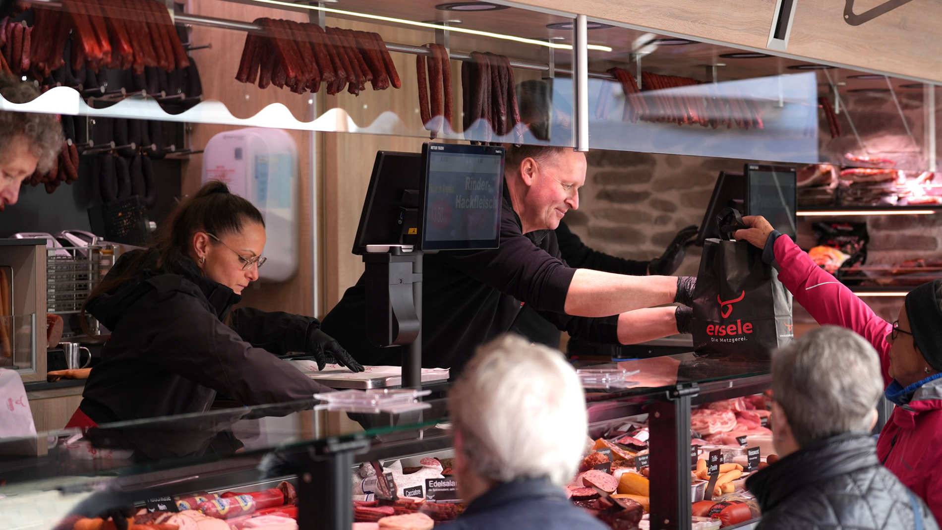 Metzgereiverkauf mit Kundschaft und Wurstwaren