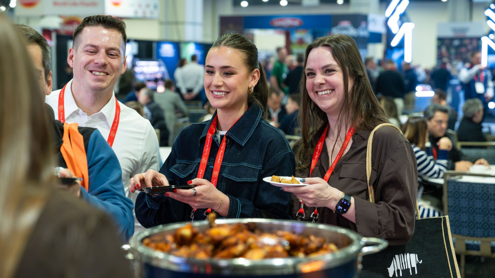 Drei Messebesucher probieren lächelnd frisch servierte Speisen an einem Stand