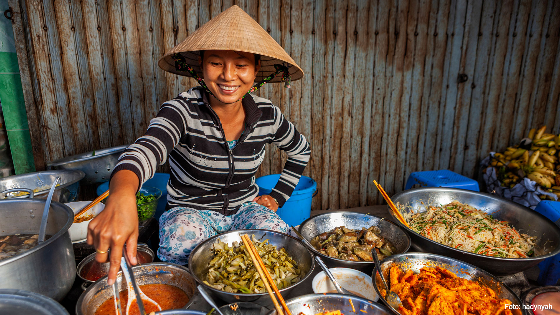 Woman wearing an Asian hat in front of her food in pans and pots